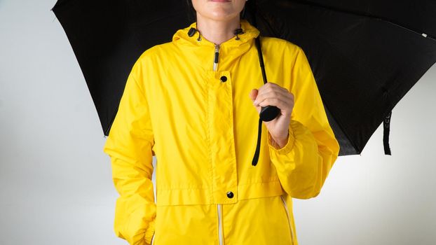 A woman in a yellow raincoat holds a black umbrella on a white background. High quality photo