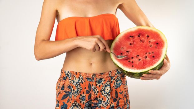 A woman in beachwear eats watermelon with a spoon - summer atmosphere. High quality photo