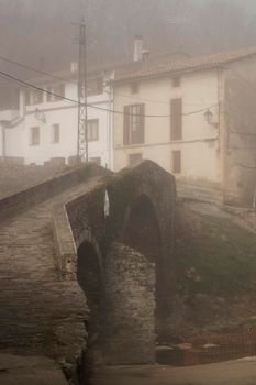 Foggy view of a medieval bridge and some houses in a small town