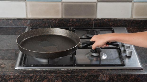 A woman's hand holds a frying pan of vegetable oil on a gas stove. High quality photo