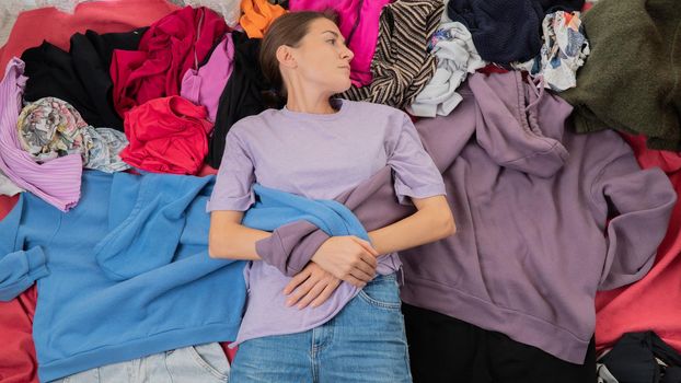 Conscious consumption of clothes - a woman lies in a pile of clothes, the dependence of a shopaholic. High quality photo