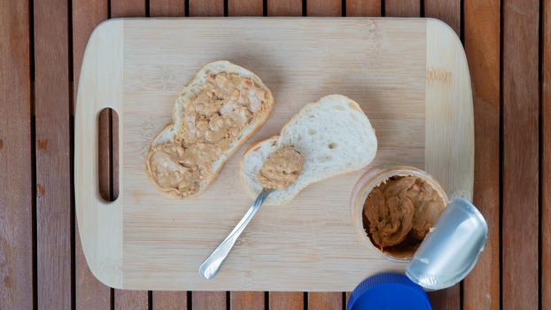 White bread sandwiches with peanut butter on a wooden background with a jar of peanut butter