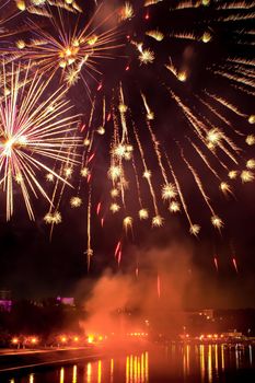 Flash of fireworks in night sky over river in city. Holiday concept. Vertical position of frame