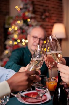 Diverse people hands clinking glasses with sparkling wine closeup, proposing christmas toast, drinking alcohol at festive dinner close view. Winter holiday celebration, xmas party