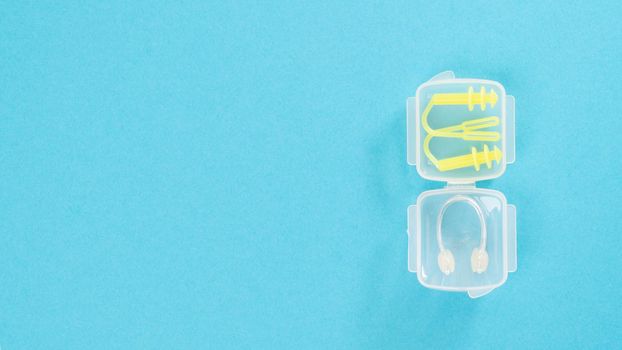 Nose clip and swimming earplug in a transparent case on a blue background. High quality photo