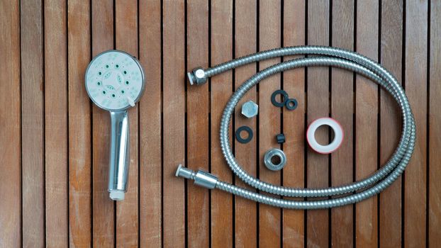 Shower head, hose, gaskets and screws for repair on a wooden background with free space under the text