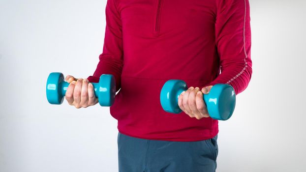 A man in a sports fom holds dumbbells on a white background. High quality photo