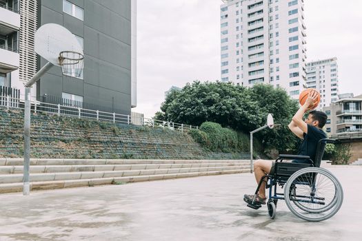 handicapped man in wheelchair playing basketball alone, concept of adaptive sports and physical activity, rehabilitation for people with physical disabilities