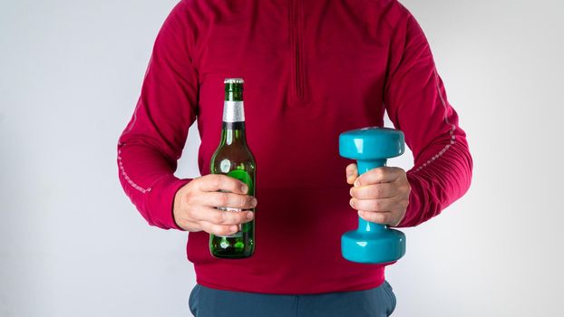 A man makes a choice between a bottle of beer and a workout with dumbbells - choose a sport. High quality photo