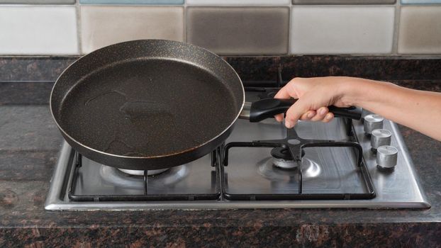 A woman's hand holds a frying pan of oil over a gas stove. High quality photo