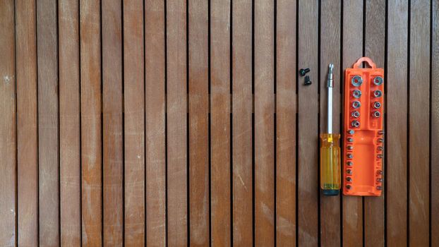 Screwdriver lies next to an orange case with bits and screws on a wooden background tool kit