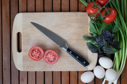 Tomatoes, green onions, basil, dill, arugula, eggs with board and knife on a wooden background. High quality photo