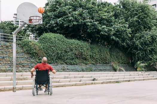 handicapped man in wheelchair playing on basket on the basketball court alone, concept of adaptive sports and physical activity, rehabilitation for people with physical disabilities