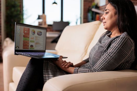 Indian person analyzing startup charts on laptop, doing remote work to plan research information and create professional report. Looking at online internet data on computer, freelance job.