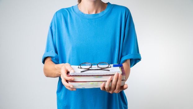 On a stack of textbooks and notebooks are glasses with transparent glasses in the hands of a student. High quality photo