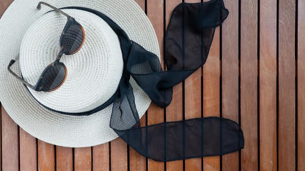 Straw women's hat with ribbon and glasses on a wooden background place for text