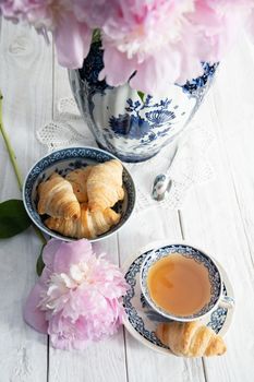 spring still life with croissants and a bouquet of pink luxurious peonies in an ancient Chinese vase with blue ornament, an antique tea cup, early breakfast or brunch, High quality photo