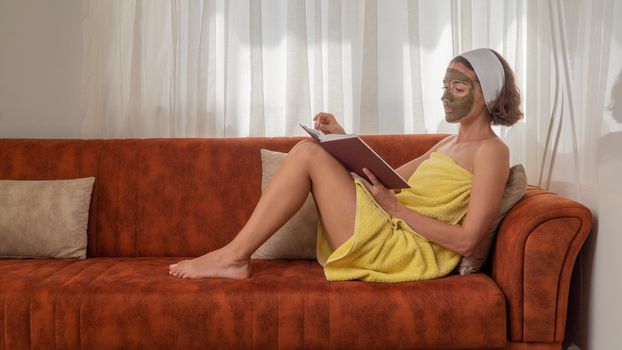 A woman with a mask on her face and in a towel reads a book on the couch - face care at home. High quality photo