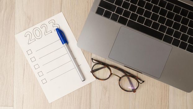 To-do list for 2023, glasses and an open laptop on a wooden table, a checklist for the new year. High quality photo