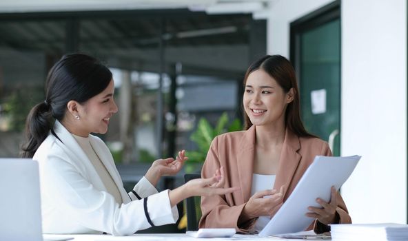 Two young beautiful asian business woman in the conversation, exchanging ideas at work..