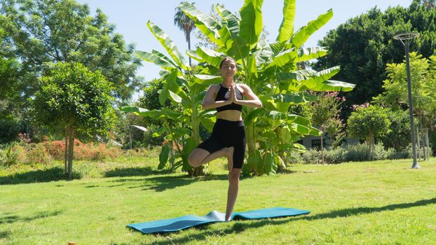 Yoga pose on one leg, a woman does yoga in the park on a sunny day. High quality photo