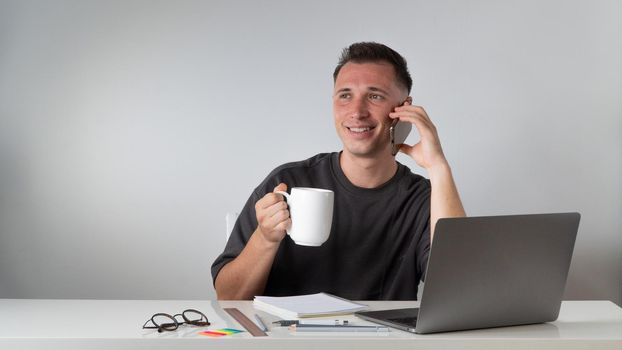 A student at a laptop talks on the phone and drinks coffee - a break for rest. High quality photo