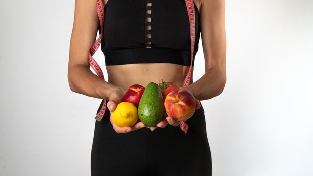 A woman in sportswear holds vegetables and fruits in her hands, a measuring tape - proper nutrition and sports. High quality photo