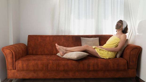 A woman with a clay face mask resting on the sofa - home self-care. High quality photo