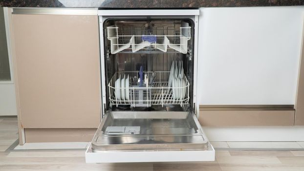 Open dishwasher loaded with half utensils