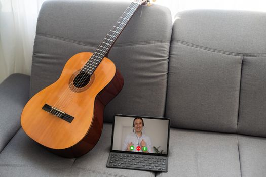 Acoustic guitar and digital tablet on a couch at cozy home background. Online music lessons, learning playing or writing songs and hobby concept.