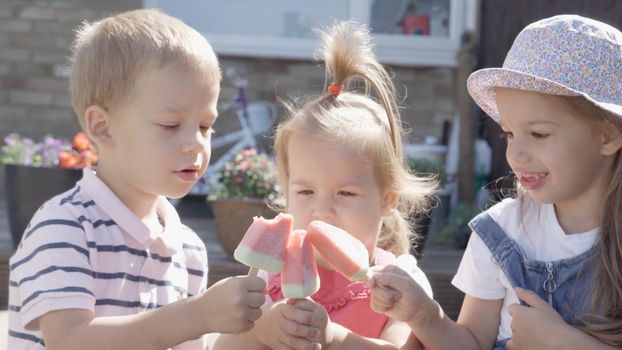 Three cute little Children enjoys delicious ice cream cone. Child eating watermelon popsicle. Kids Siblings snack sweets in Home Garden. Summer holiday Hot weather Sunny Day. Childhood, Food Candy.