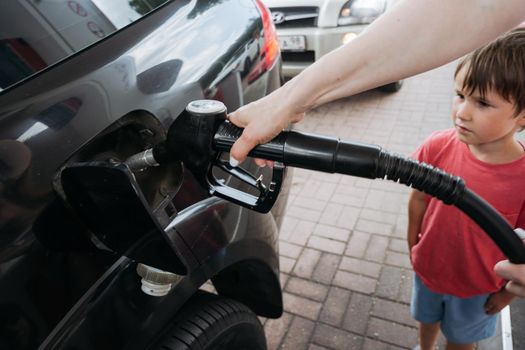 Closeup of a Fueling a car at the gas station. Small boy is standing. next to the car and looking