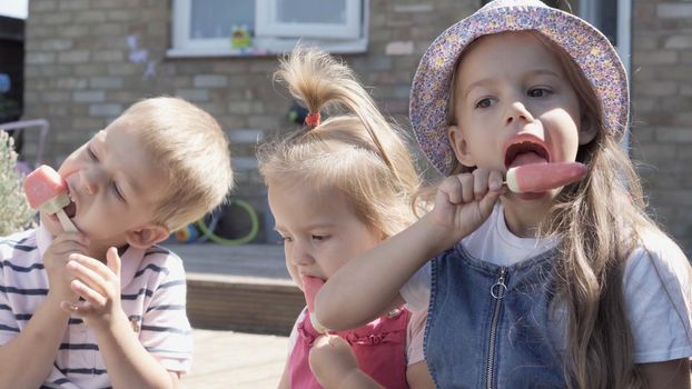 Three cute little Children enjoys delicious ice cream cone. Child eating watermelon popsicle. Kids Siblings snack sweets in Home Garden. Summer holiday Hot weather Sunny Day. Childhood, Food Candy.