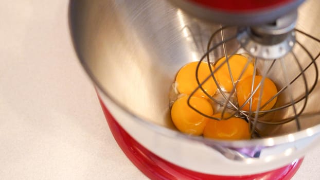 Raw eggs in a metal bowl of standing mixer. Preparing egg yolk with sugar in kitchen mixer