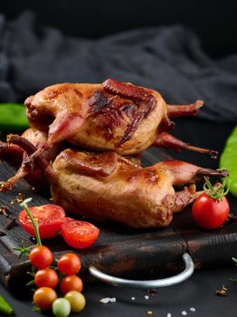 Frying carcasses of quails lie on a wooden board with vegetables, a black table