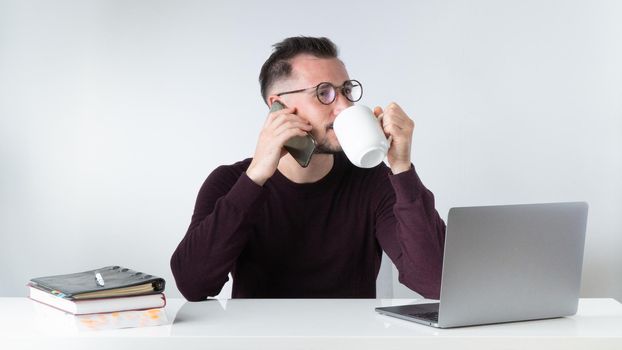 A man in the office drinks coffee or tea and talks on the phone - work environment. High quality photo