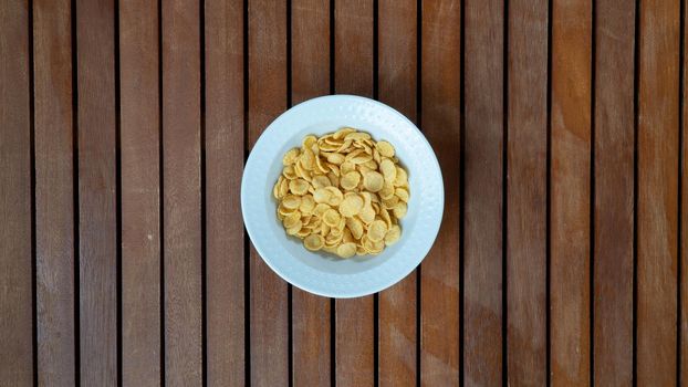 Corn flakes in a white plate in the middle on a wooden background for breakfast. High quality photo