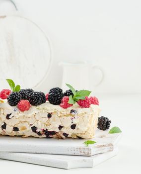 Baked meringue roll with cream and fresh fruits on a white wooden board, delicious dessert