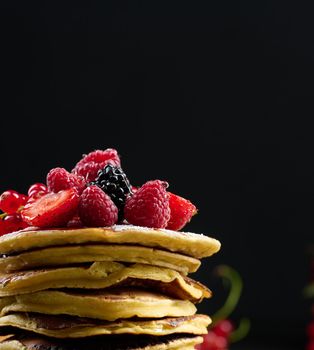 A stack of pancakes with fresh fruits poured with syrup on a black background