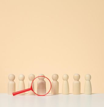 Wooden figures of men stand on a beige background and a blue plastic magnifying glass. Recruitment concept, search for talented and capable employees, career growth