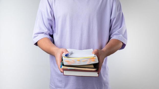 Male student holds a stack of notebooks and books on a white background. High quality photo