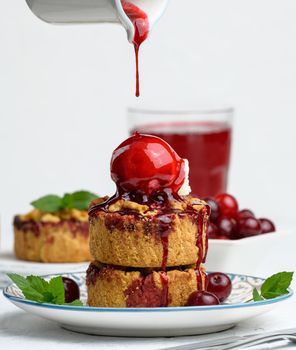 Cherry crumble pie decorated with a scoop of ice cream and poured with cherry sauce on a plate, white background