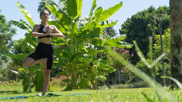 A woman does yoga in the park, stands in a pose on one leg. High quality photo