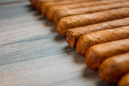 Cuban cigars on rustic wooden table in line on the edge of background.