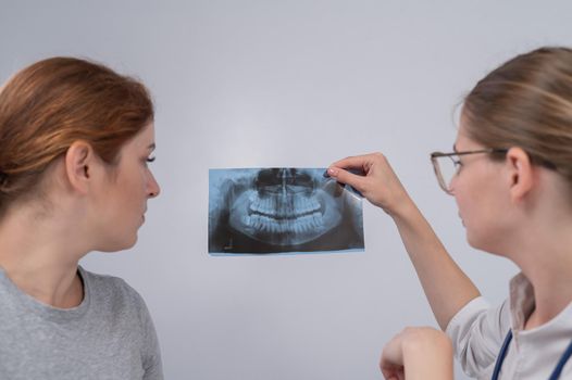 A woman doctor and a patient at the reception are discussing an x-ray of the jaw