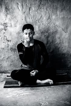 Portrait shot of the young man doing pranayama or pranayam or breath control yoga on a colorful mat with wearing black attire.