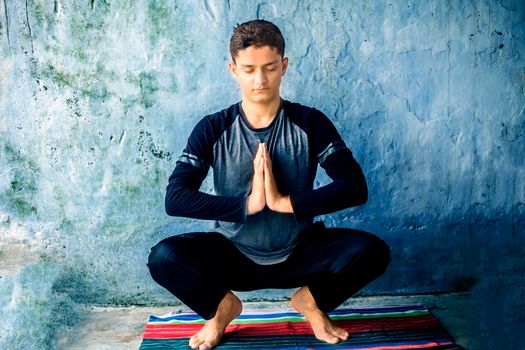 Teenage boy wearing black colored attire and doing yoga on colorful traditional mat and doing famous Garland pose or Malasana. Horizontal shot.