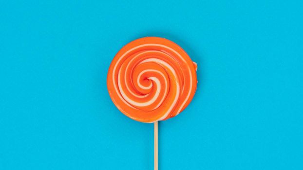 Round orange lollipop on a stick on a blue background - juicy sweet background. High quality photo