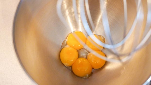 Raw eggs in a metal bowl of standing mixer. Preparing egg yolk with sugar in kitchen mixer