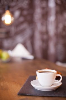 Minimalist composition of a cup of coffee on a black stone plate with blurred background. Tasty coffee. Vintage pub.